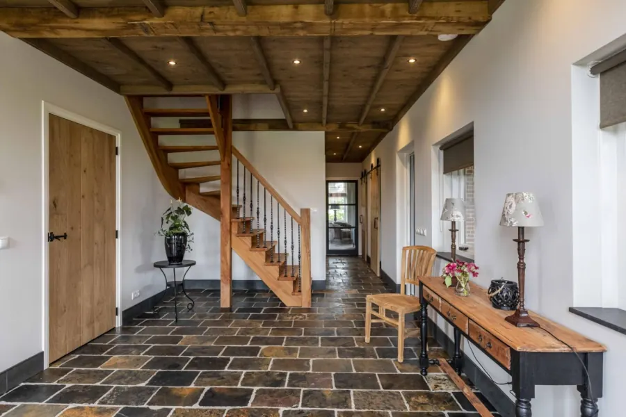 Hal met natuurstenen vloer en houten trap naar de slaapkamers